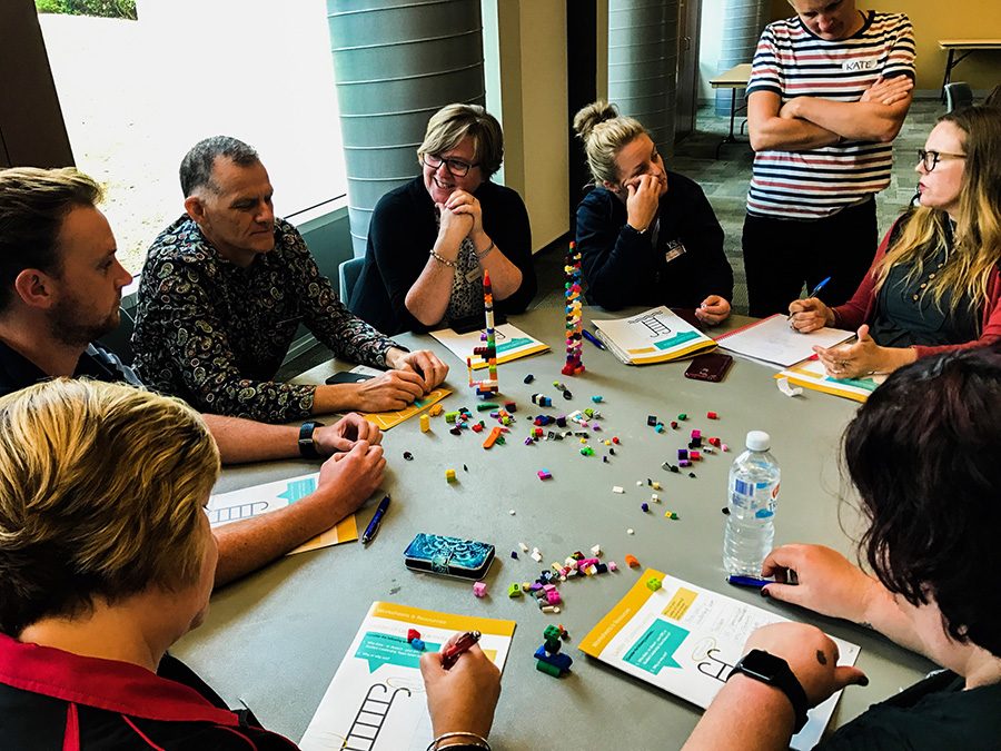 A group of adults sits around a table with piles of Lego blocks