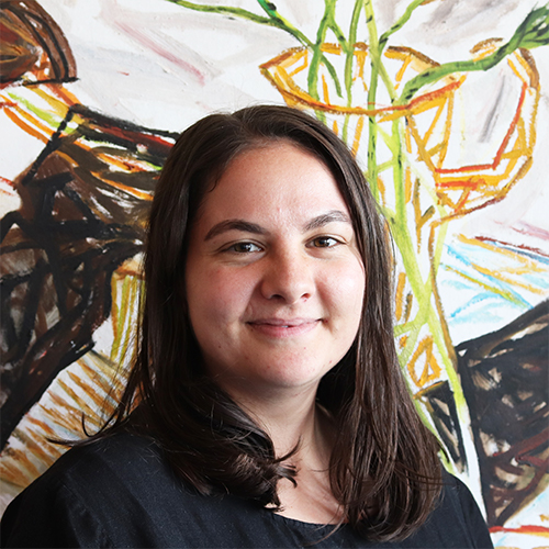 Hayley, a young woman with shoulder-length brown hair in a black dress standing in front of a painting.