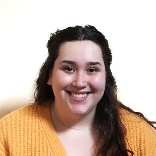 Keisha, a young woman with dark wavy hair wearing a yellow cardigan.